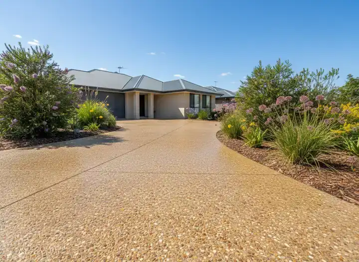 concreting toowoomba: curving exposed-aggregate concrete driveway with a pebble finish beside a brick house and garden beds